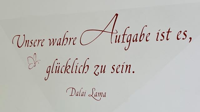 Zitat des Dalai Lama: "Unsere wahre Aufgabe ist es, glücklich zu sein." Wandtatoo, gesehen und fotografiert in einem Hotelzimmer
