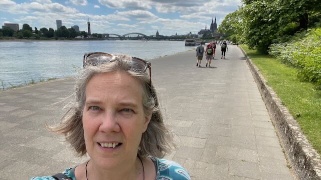 Mut-Tour-Wanderung 2025: Sabine Musseleck am Rhein-Ufer mit Wandergruppe der Großen Mut-Wanderung und Kölner Dom im Hintergrund